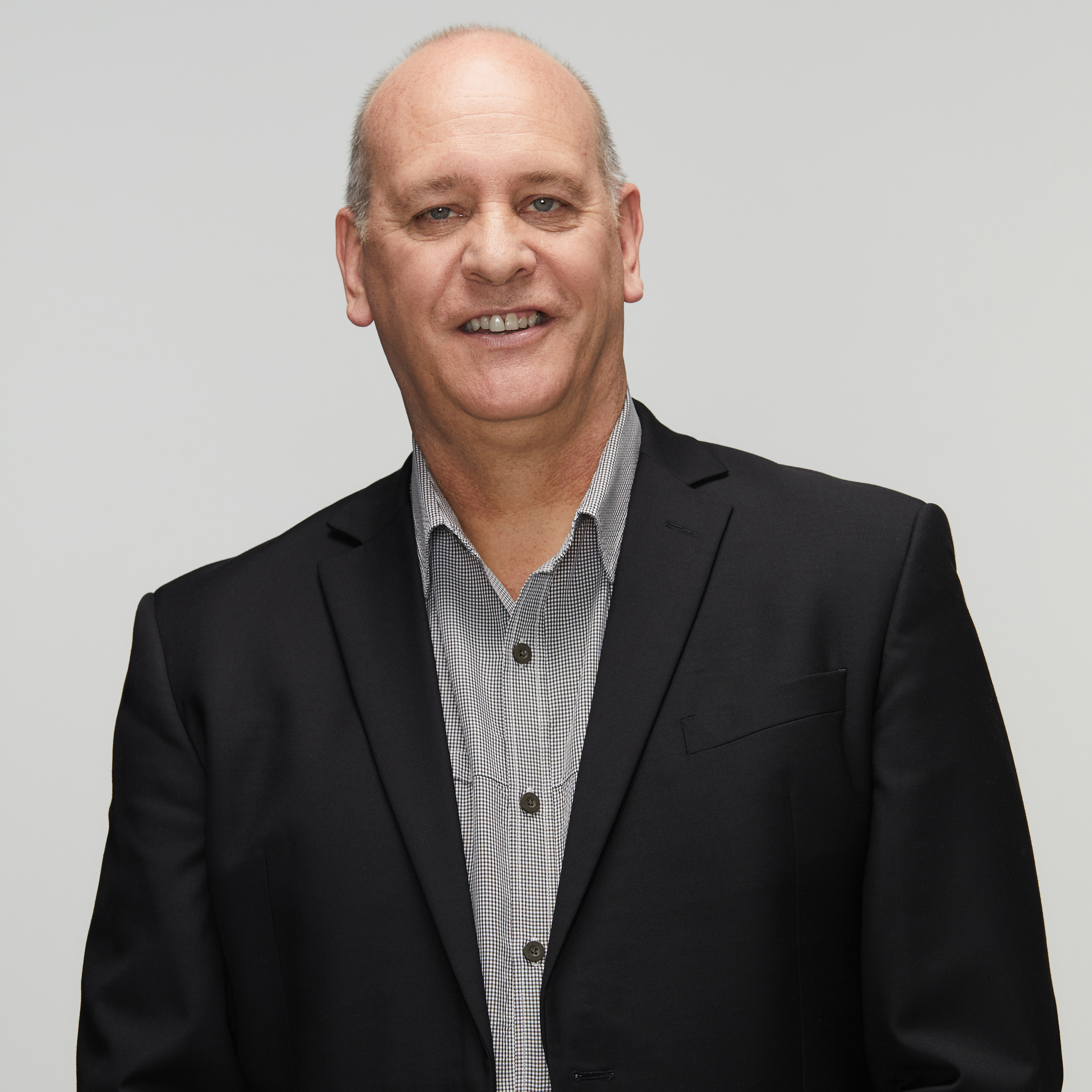 Jim's story Image of current police chaplain smiling at the camera wearing a grey and white pattern shirt with a navy suit jacket on top. Late forties, male with light skin and light, receding hair.