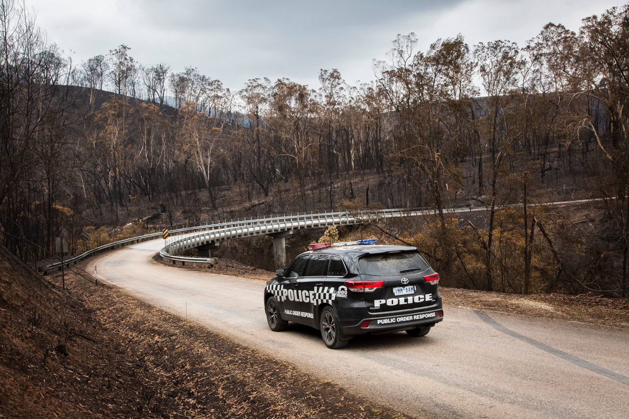 Lone police car driving through bushfire affected disaster zones.