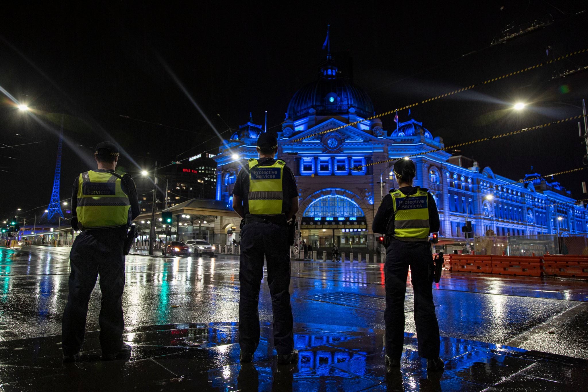 Protective services officers outside Flinders St Station, Melbourne at night. The station has been lit with blue lighting as a tribute following the Kew tragedy