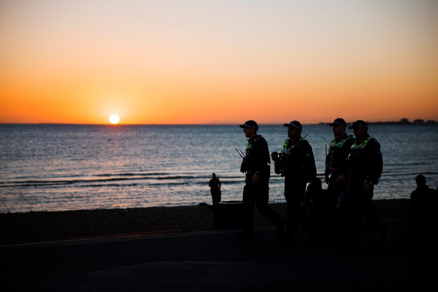 Four uniformed police officers patrolling the beach at sunset.