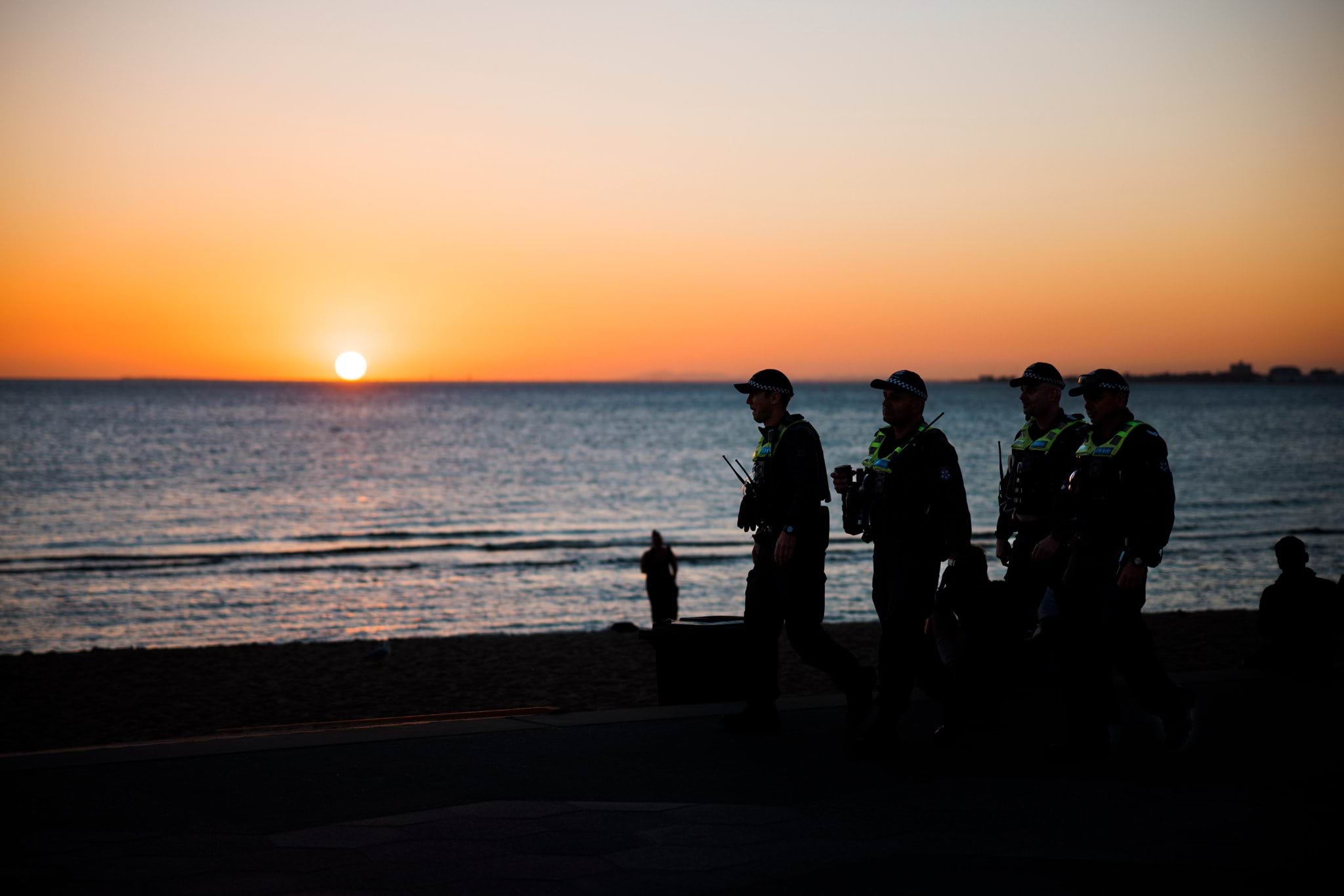 Four uniformed police officers patrolling the beach at sunset.