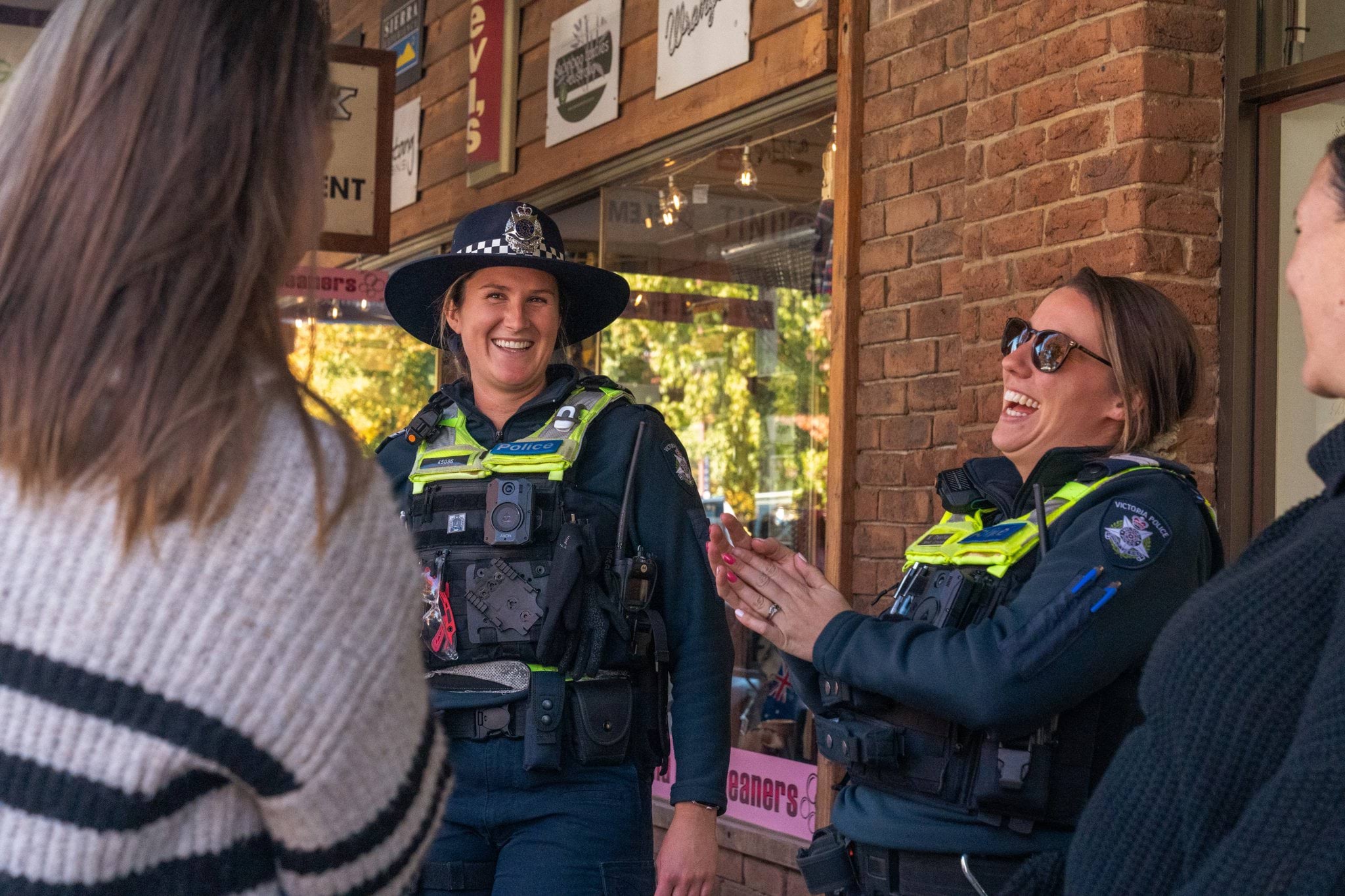 Two female police officers in blue uniforms, and yellow safety vests chatting in the street with members of the community.